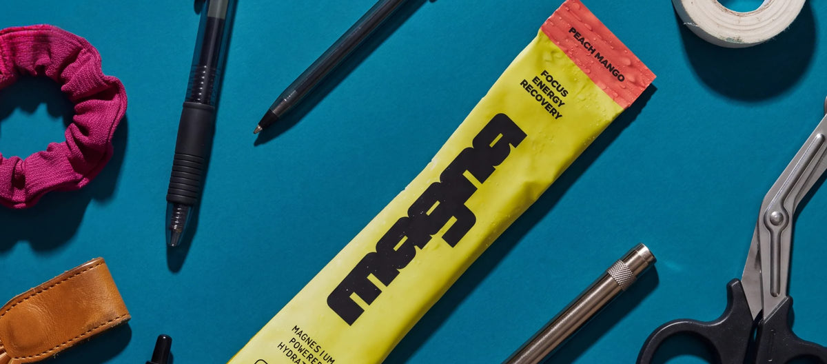 Magna Peach Mango stick on a blue surface with pens, medical tape, trauma shears and a scrunchie