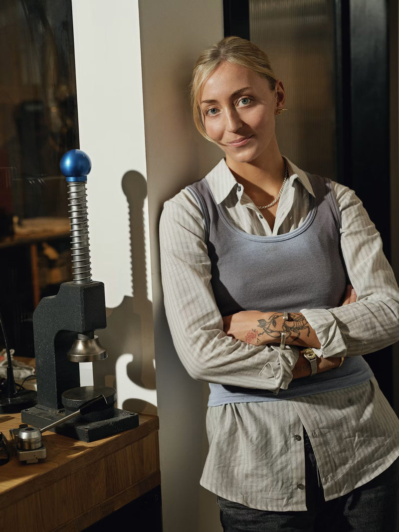 Smiling tradeswoman in a work apron leaning by a machine in her workshop