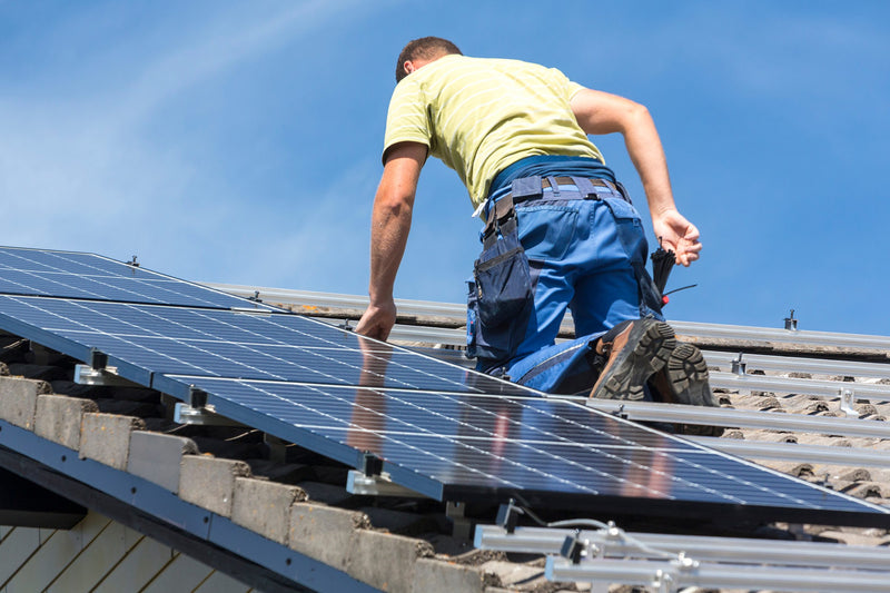 Worker installing solar panels on a sunny roof