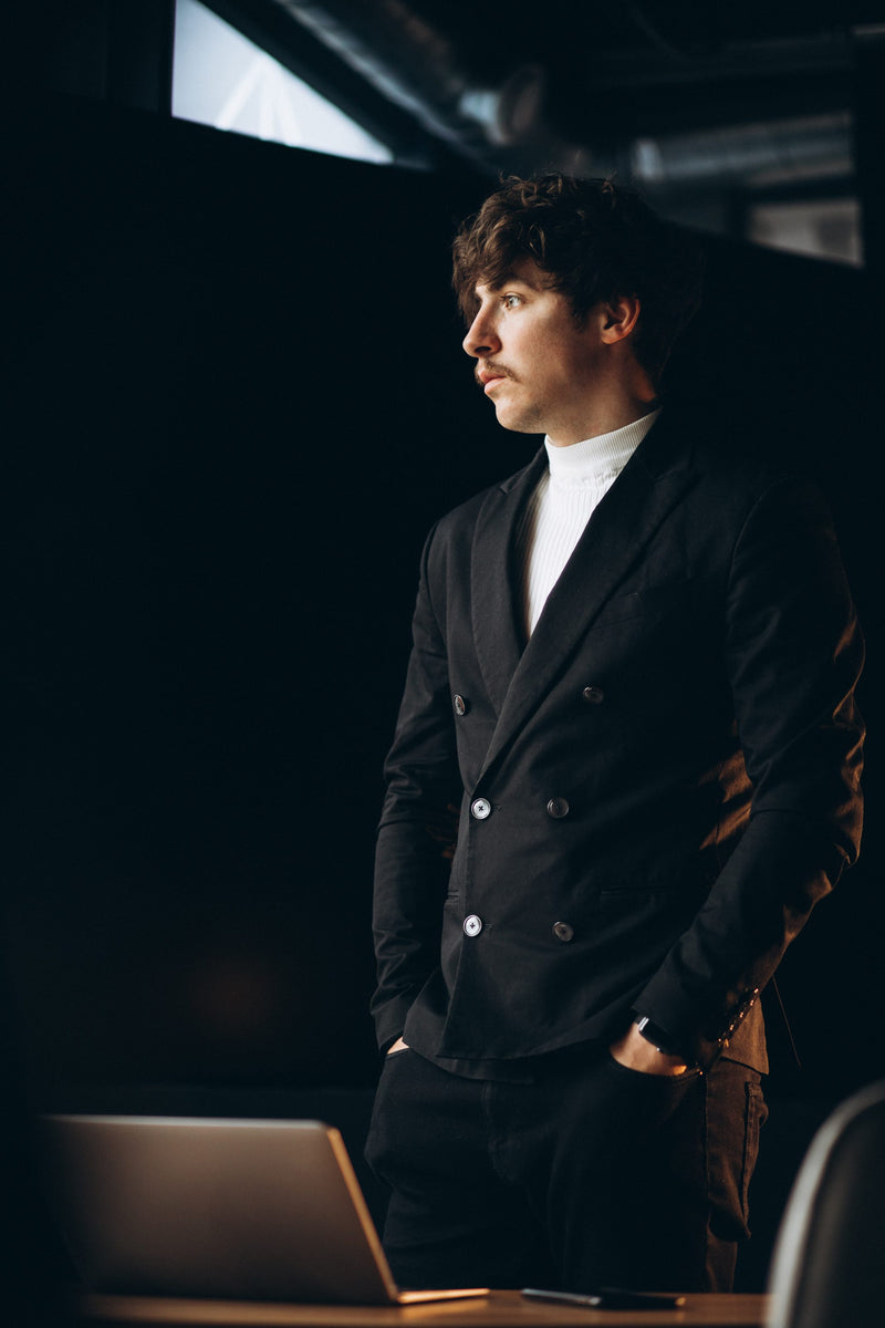 Young man in a black jacket standing in a dark studio