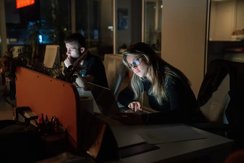 Two night shift workers at their screens in a dark office