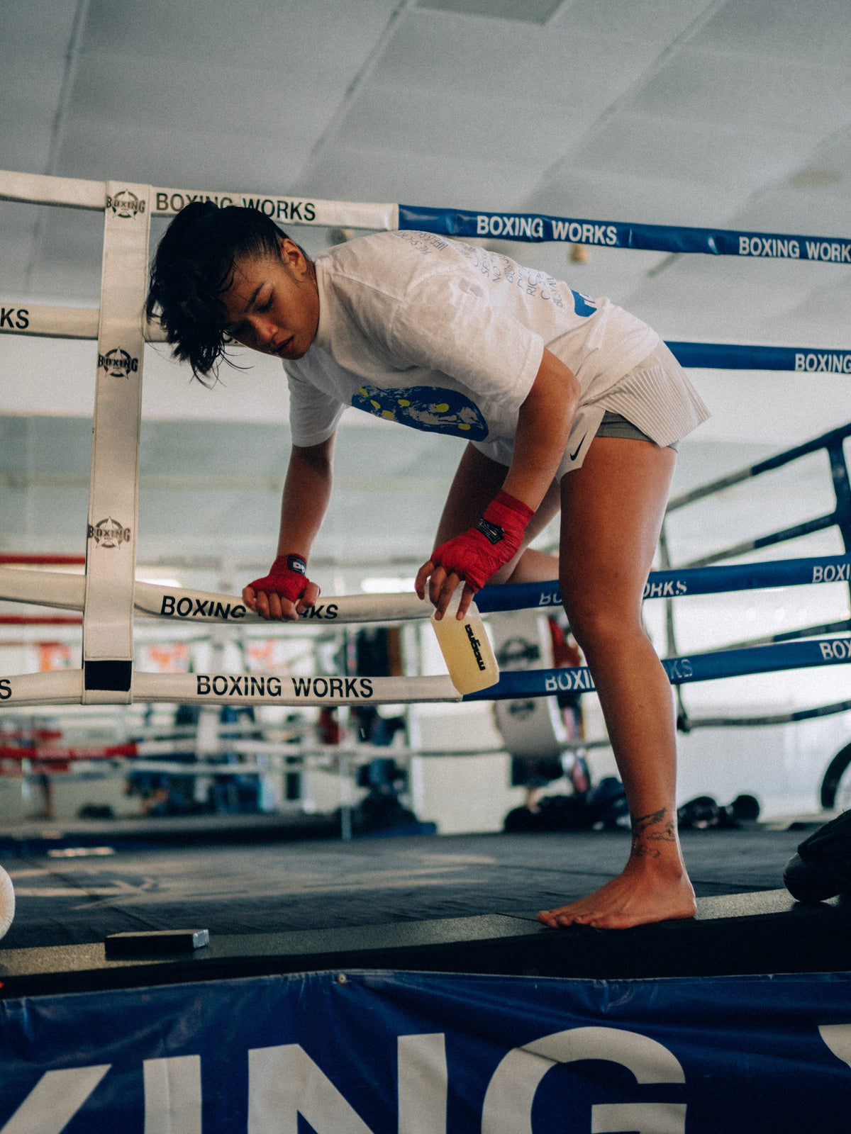 Athlete with wrapped hands leaning on boxing ring ropes, holding a Magna stick pack