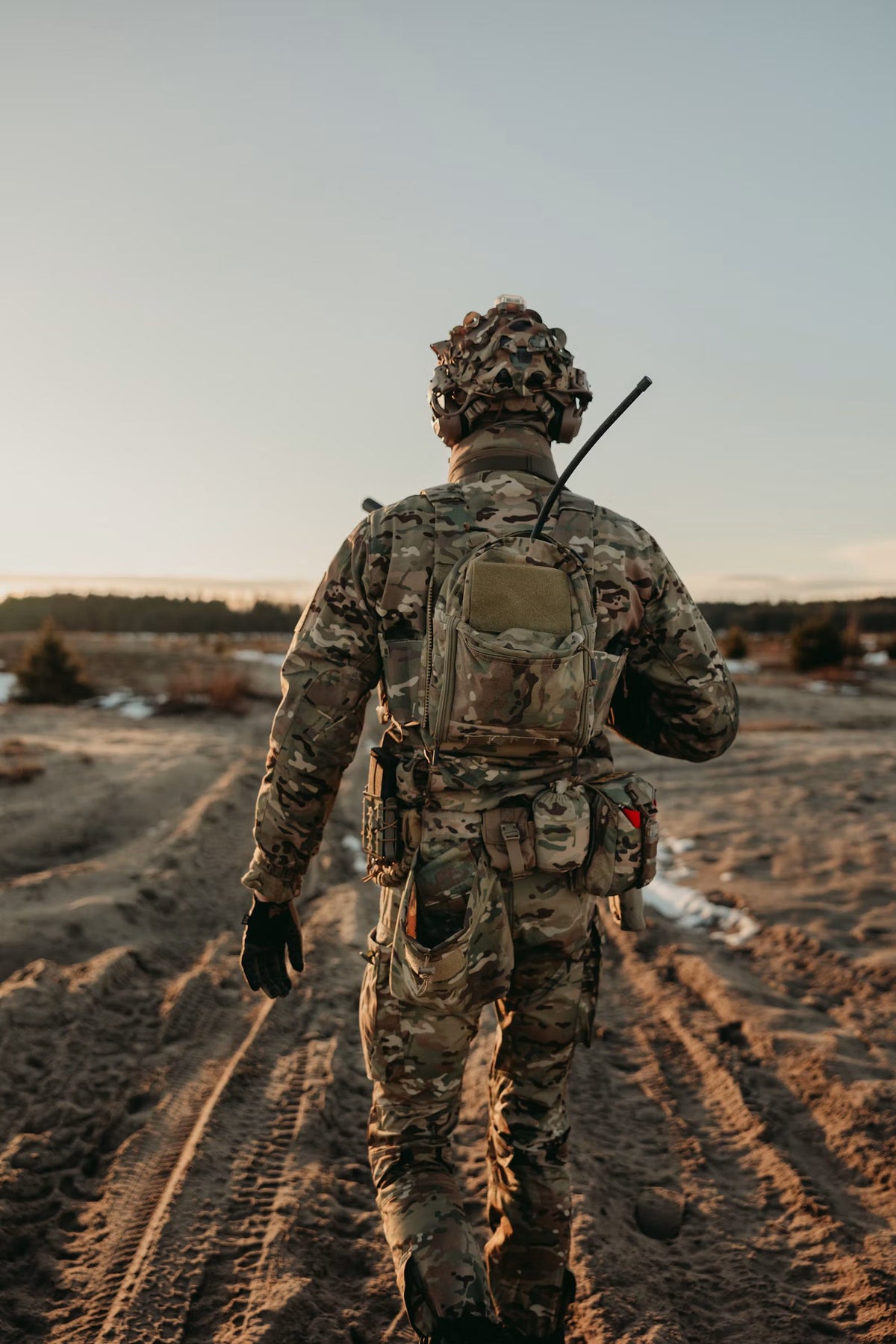 Soldier in camouflage gear walking across open terrain at dusk