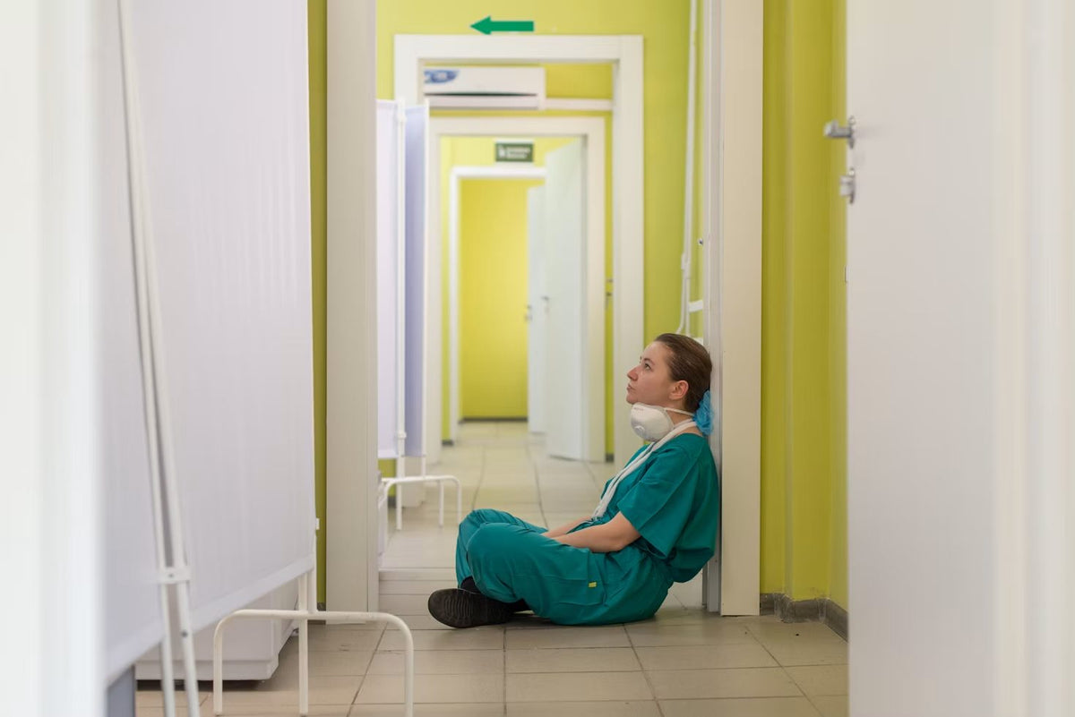 Nurse in scrubs resting on the floor of a hospital corridor
