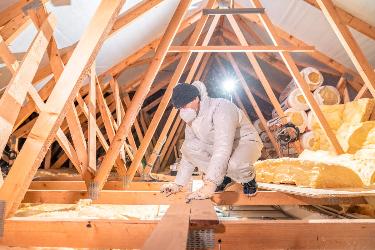 Worker in a protective suit and mask installing insulation in an attic
